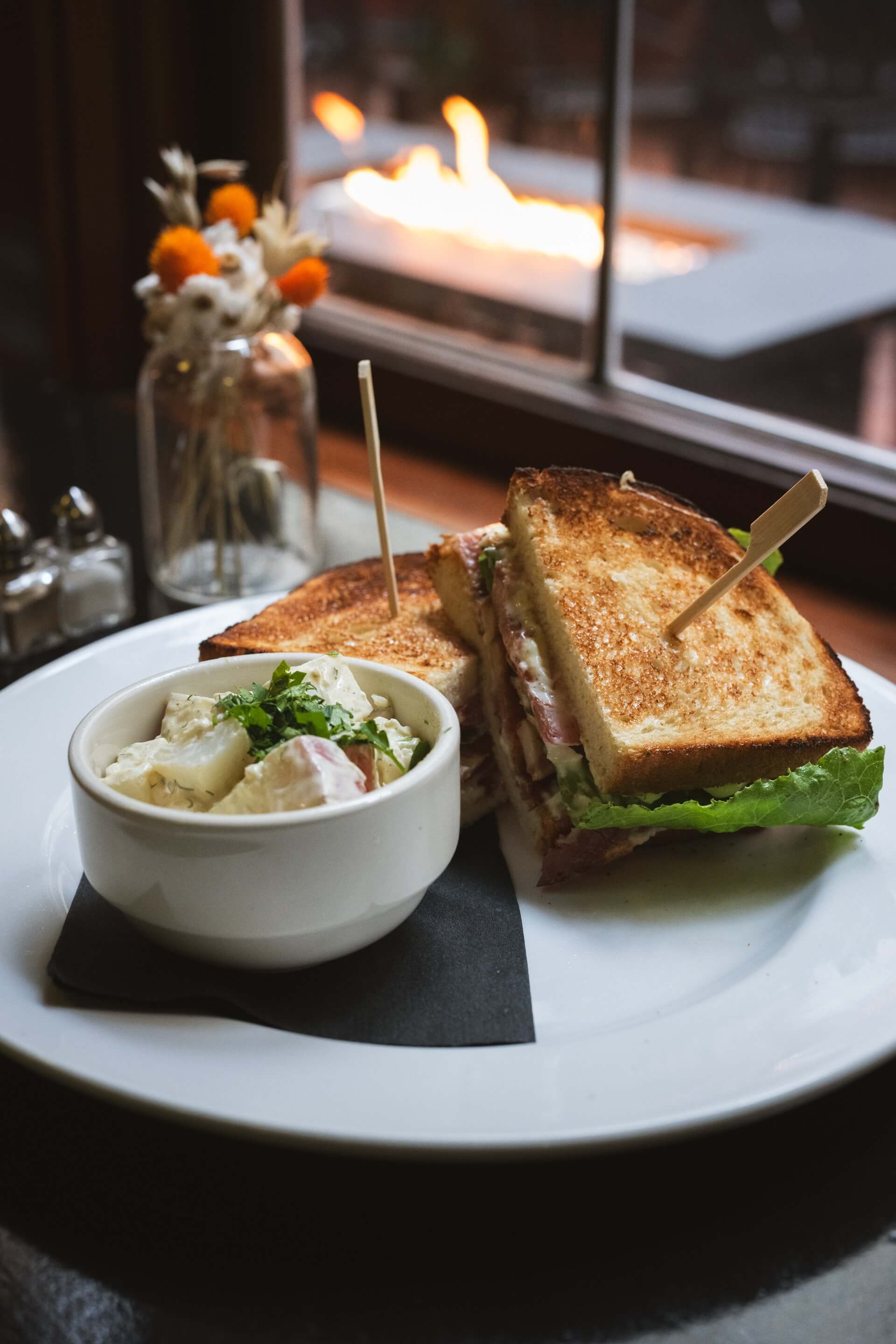 A plate with a sandwich and a bowl of salad in front of a fireplace.