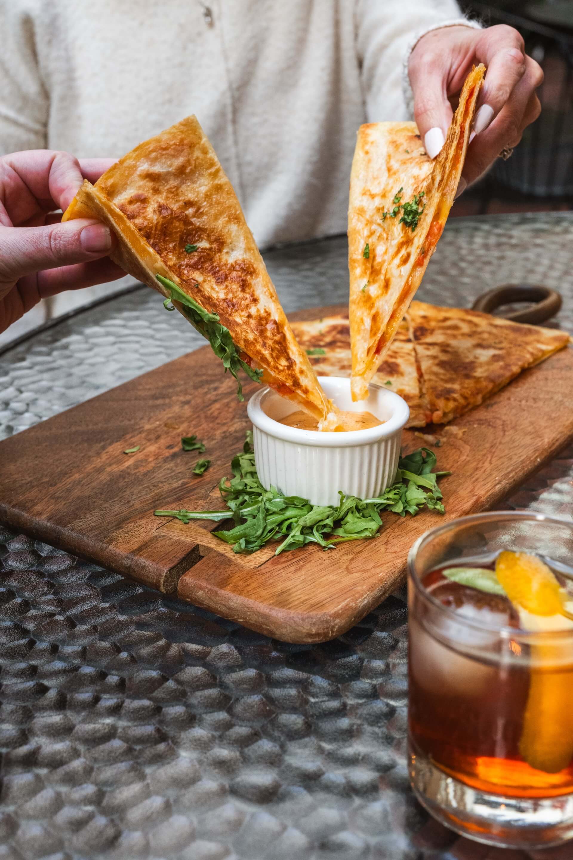 a person dipping a quesadilla into a dip on a wooden board